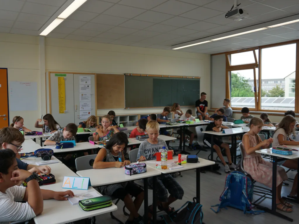 Kinder sitzen in Reihen an Einzeltischen.
